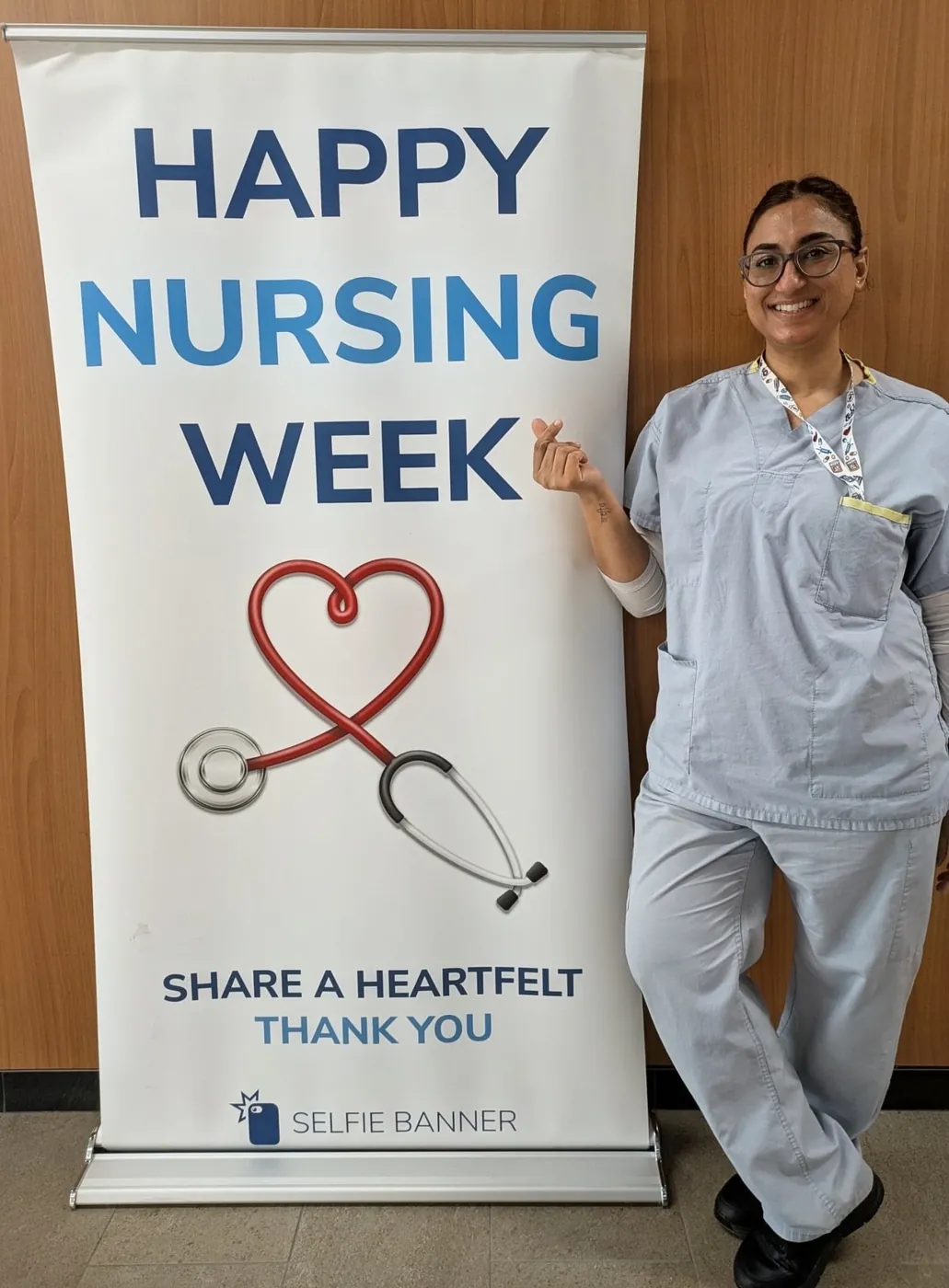 Jasraj in scrubs beside a Happy Nursing Week banner