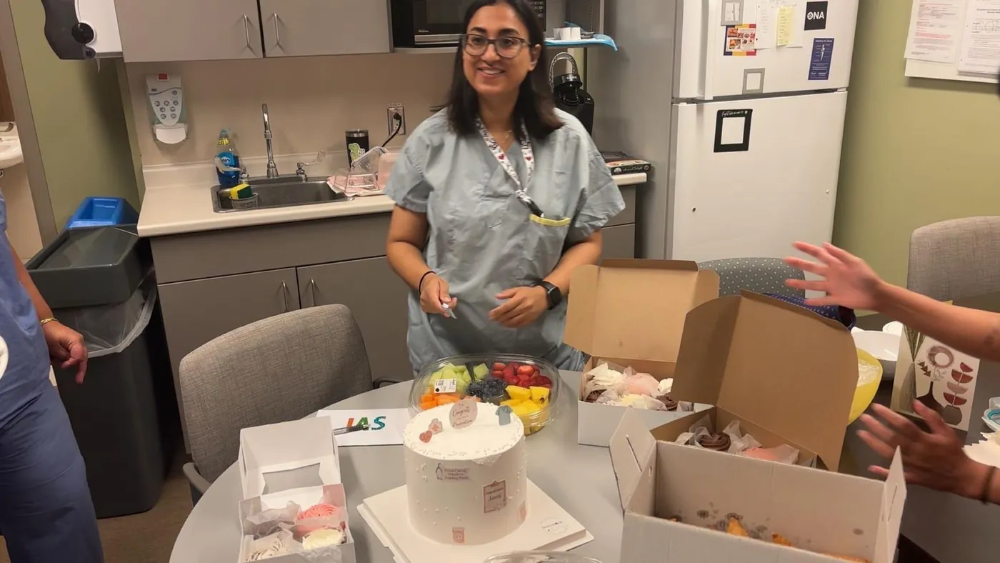 Jasraj in scrubs smiling at a table with a cake and treats in the staff room